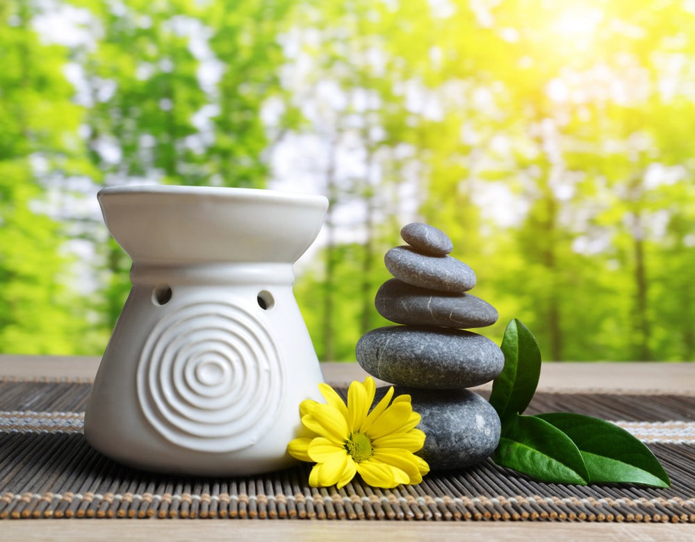 essential oil burner with zen rocks and flower and trees in background